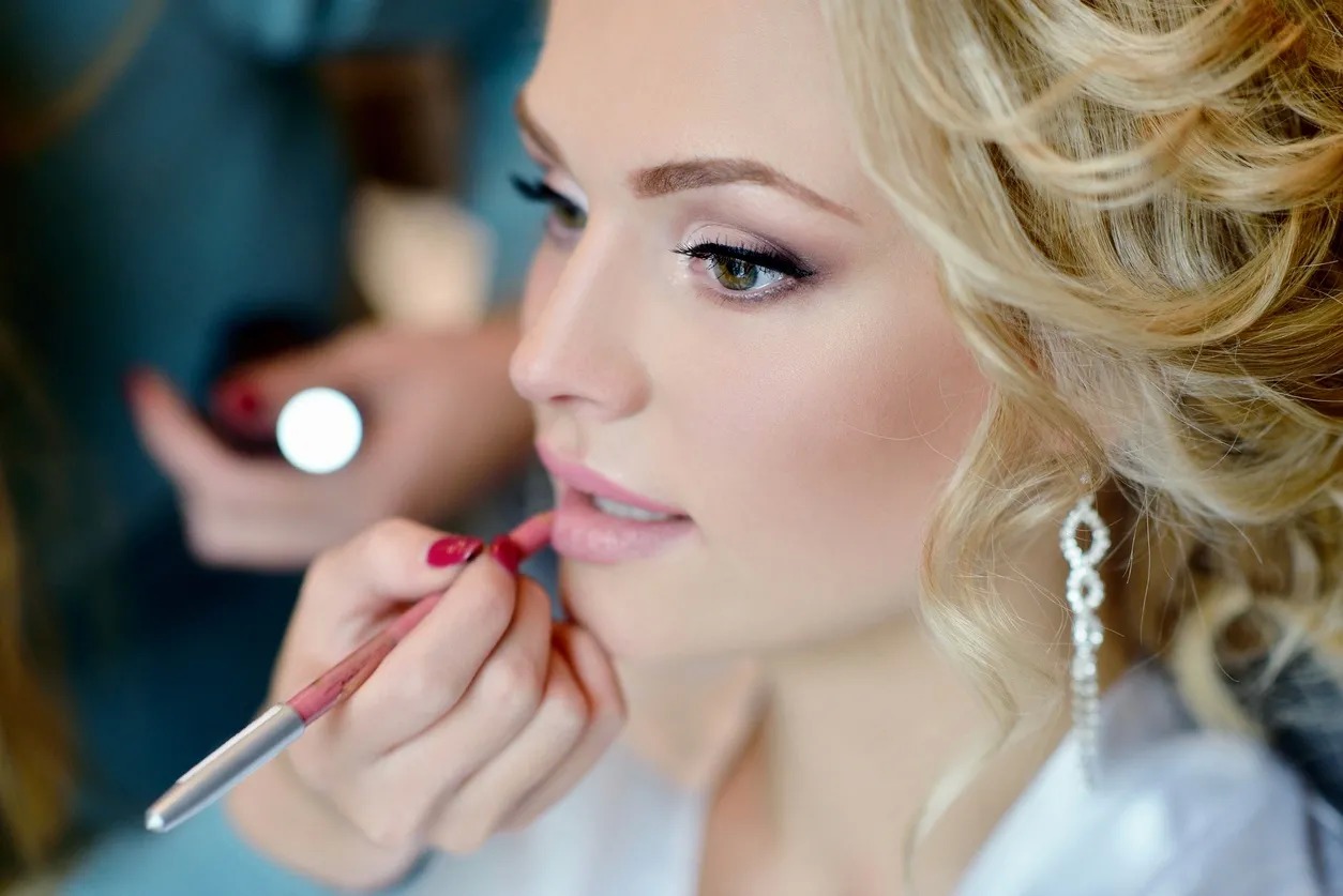 A woman is putting lipstick on her lips.